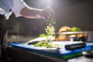 A chef sprinkles herbs on a dinner plate at a restaurant.